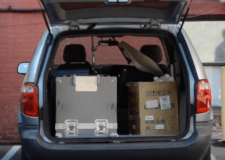 Open trunk of the blue Guerrilla Eye Service minivan with equipment inside. 
