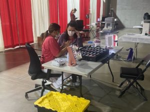 Two volunteers sit together at a folding table covered with eyeglass frames.
